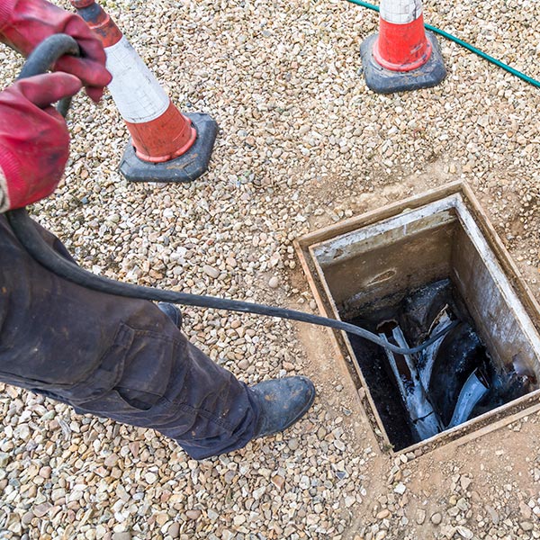 Man unblocking sewage drain through open inspection chamber