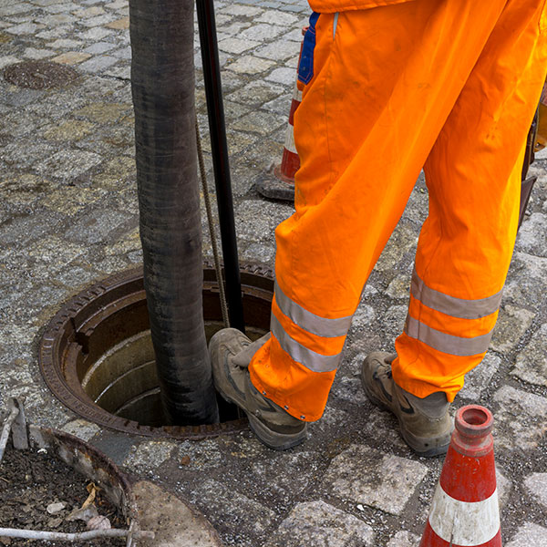 sewerage worker on street cleaning pipe